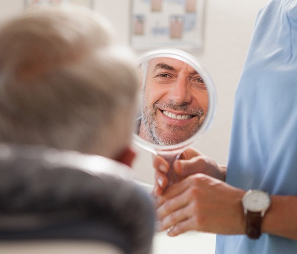 Man smiling while looking at reflection in handheld mirror