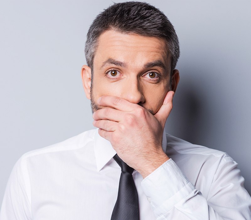 Man in need of gum disease treatment covering his mouth