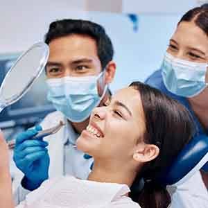 Patient smiling at reflection with dentist and dental assistant