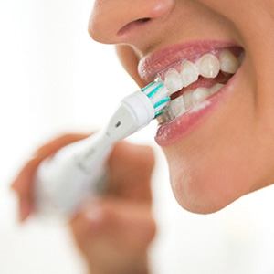 A woman using an electric toothbrush to thoroughly clean her teeth in the morning