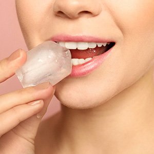 A woman holding a large ice cube and preparing to bite down on the corner of it