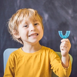 A little boy wearing a yellow shirt and holding a blue mouthguard to protect his teeth