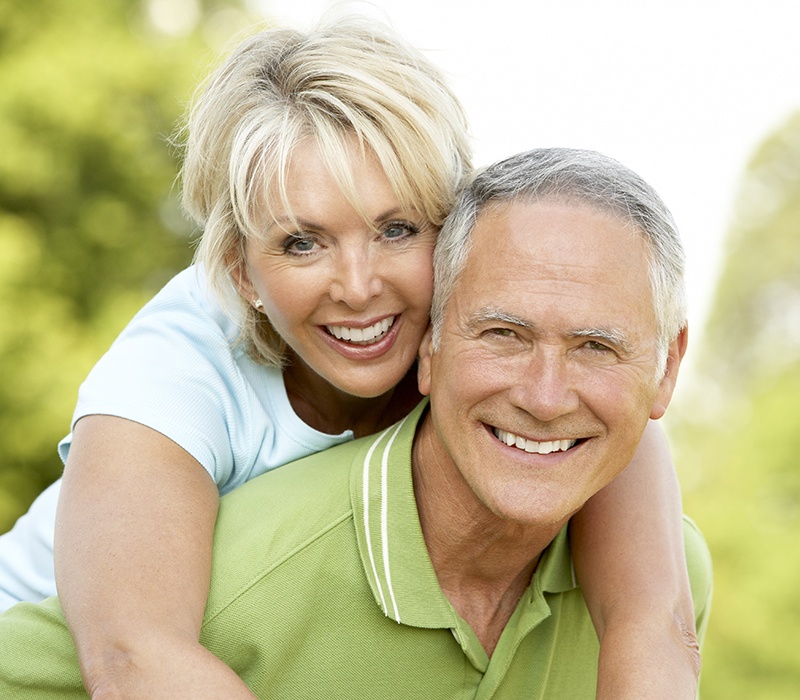 Older man and woman smiling after replacing missing teeth