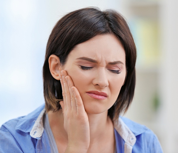 Woman in need of TMJ therapy holding jaw