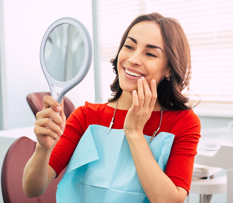 Woman looking at smile after porcelain veneer treatment