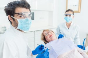 a female patient lying back in the chair while the dentist and dental hygienist, both wearing personal protective equipment, look on