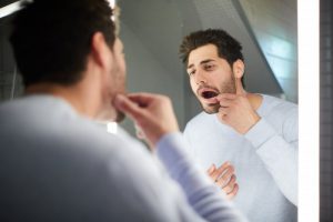 man looking at his mouth in a mirror to see if he needs to replace dental fillings