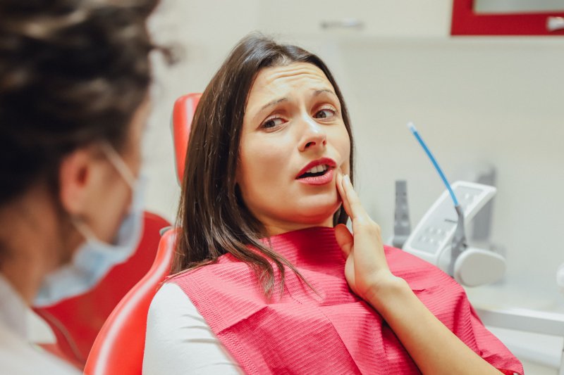 a female patient holding her mouth in pain while listening to her dentist