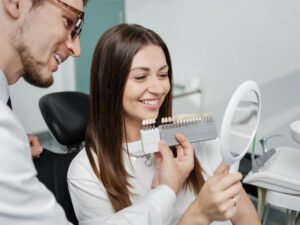 Young woman in dentist's chair smiling into mirror looking at veneers. 